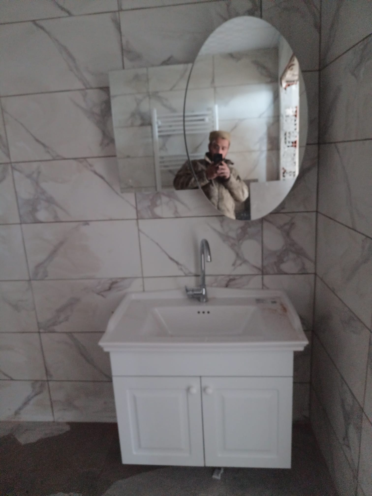 Mermer desenli banyoda dolaplı lavabo, batarya ve oval ayna montajı